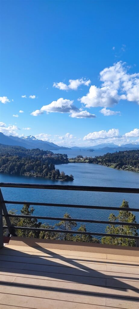 Lago entre florestas e montanhas, visto de um mirante com guarda-corpo